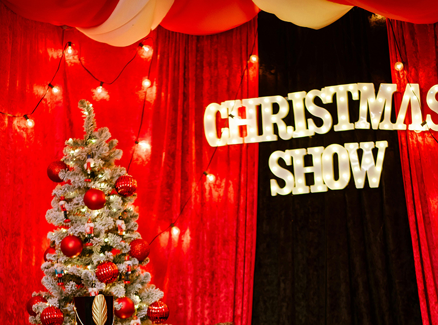 christmas show in light up letters with a red curtain and Christmas tree